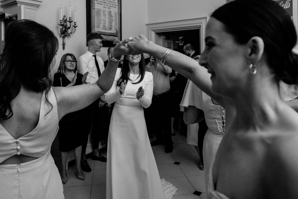Black and white photo of people dancing and celebrating at a formal event with guests watching nearby.