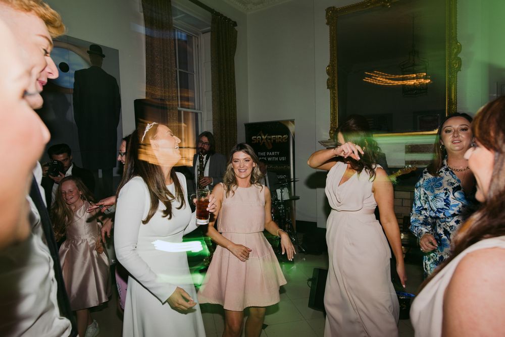 A group of party guests dancing together in a lively indoor celebration with a green-tinted atmosphere.
