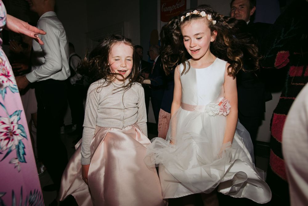 Two young attendees in formal dresses sit together during an evening celebration event.