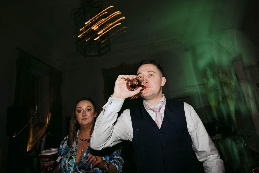 Dimly lit reception scene with party guests and moody green lighting at a wedding celebration.