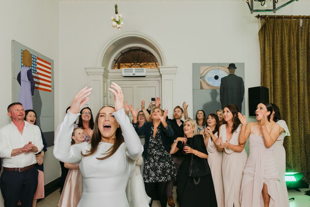 Wedding guests celebrate with joy and raised hands during a reception in an elegant room with an American flag.