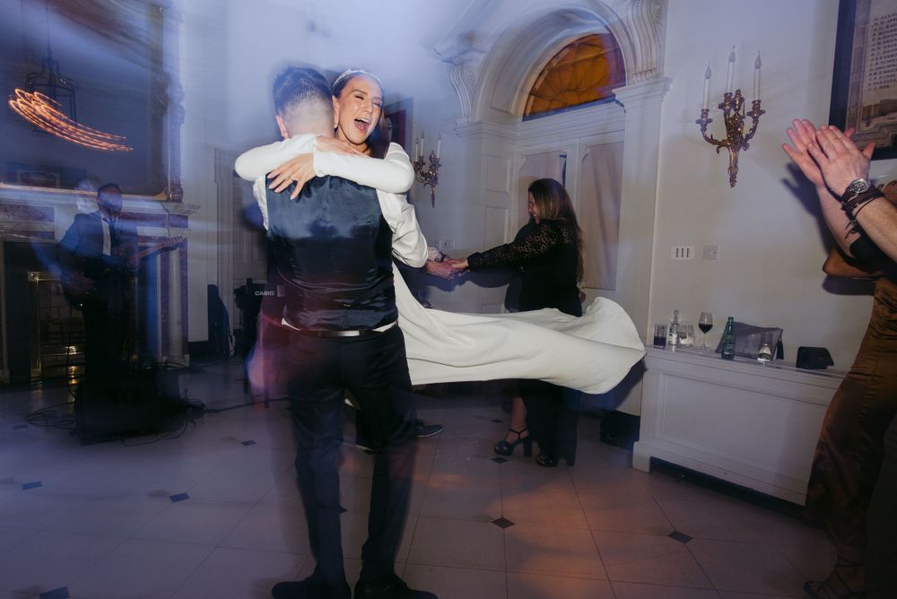 A couple dances together during a wedding reception in an elegant white room with arched doorways.