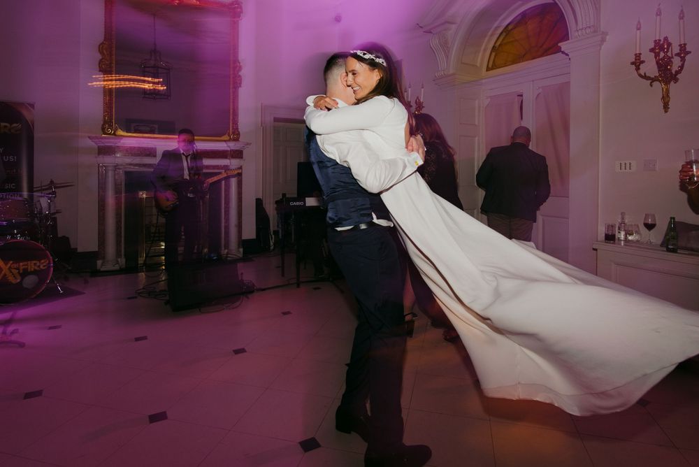 A couple performs a dramatic dance dip under purple lighting during their wedding reception.
