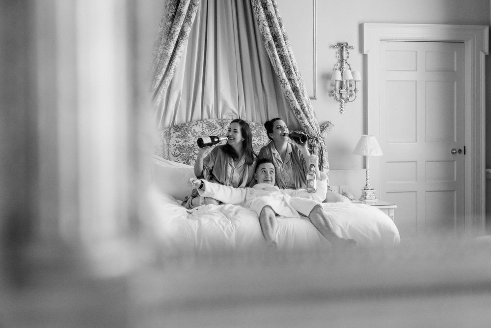 Black and white photo of people sitting together on a bed in a bedroom, viewed through foreground elements.