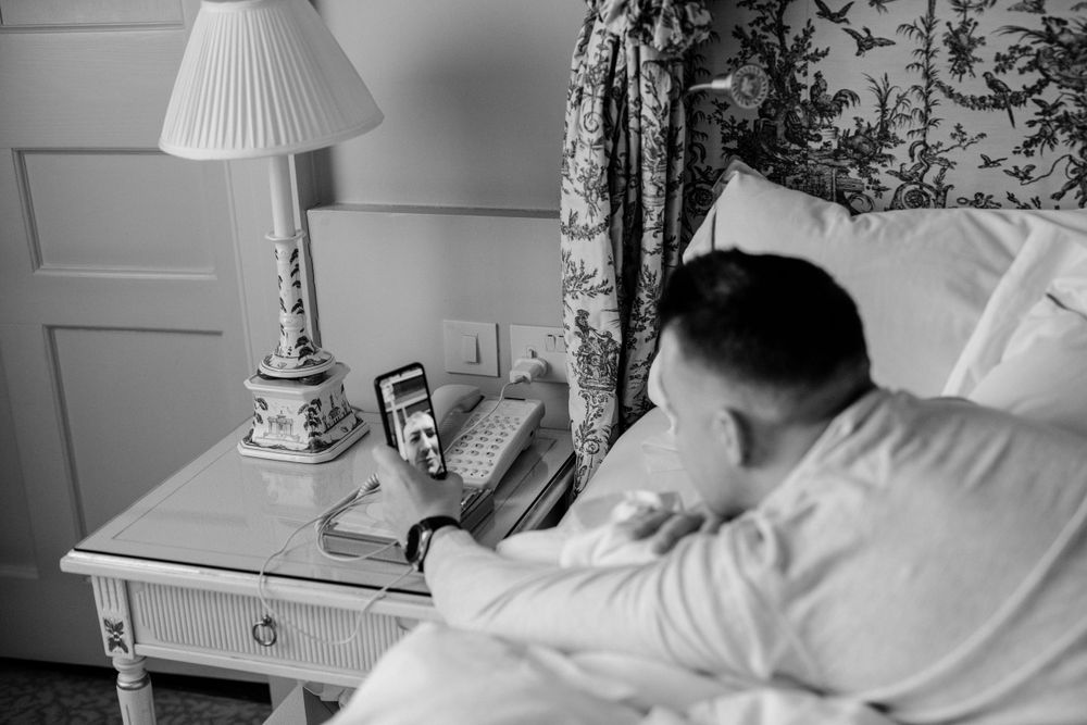 Person lying in bed next to vintage table lamp and rotary telephone in black and white photograph.
