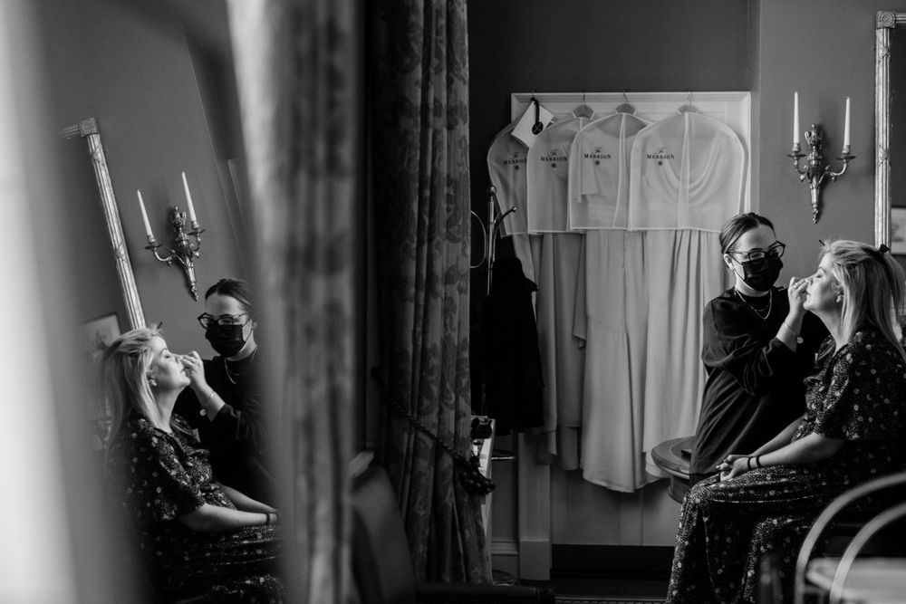 Black and white photo of figures holding candles during an intimate indoor ceremony with reflections in a mirror.