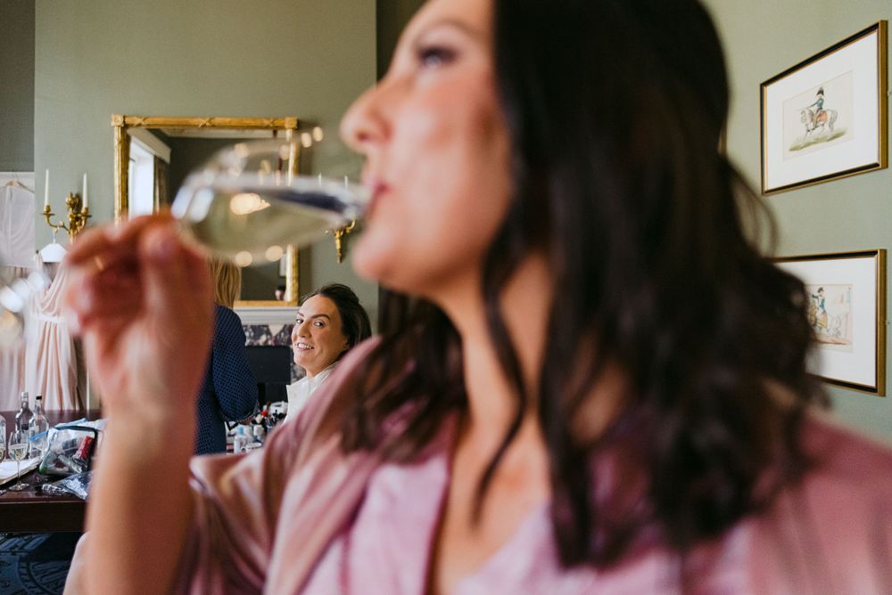 Woman with long dark hair taking a drink in a room with framed artwork on the walls.