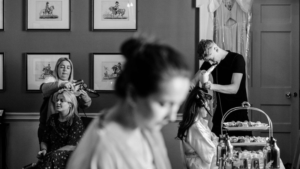 Black and white candid scene from a wedding preparation moment with activity in an elegant room with framed artwork.