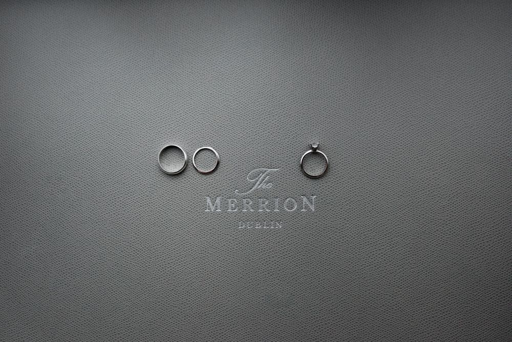 Three wedding rings displayed on gray background with Merrion London logo.