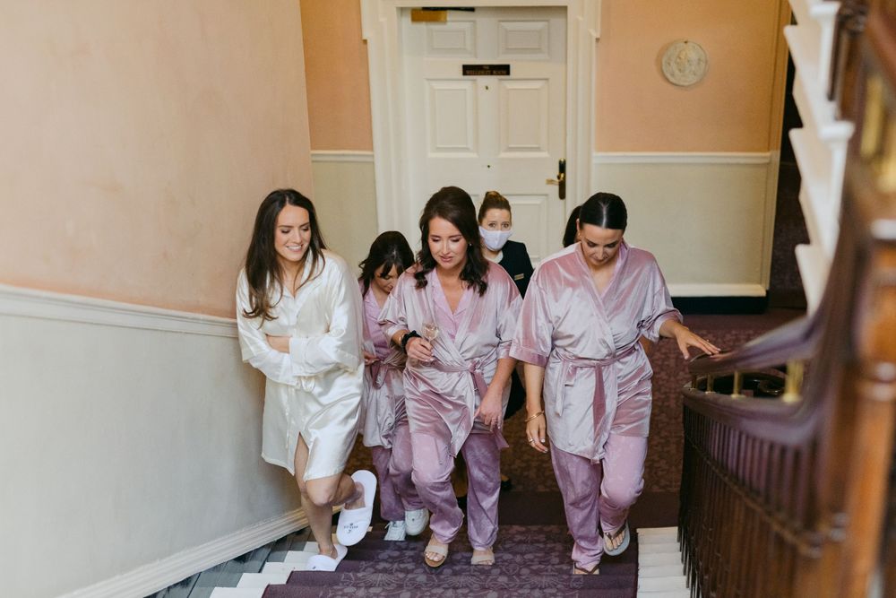 A group in matching pink and white satin robes walks down a carpeted staircase together.