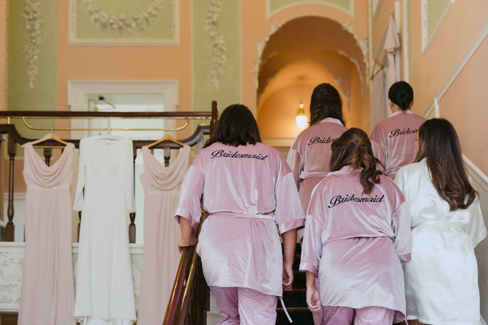 A group in pink robes stands looking at wedding dresses hanging on a wall in preparation for a bridal event.