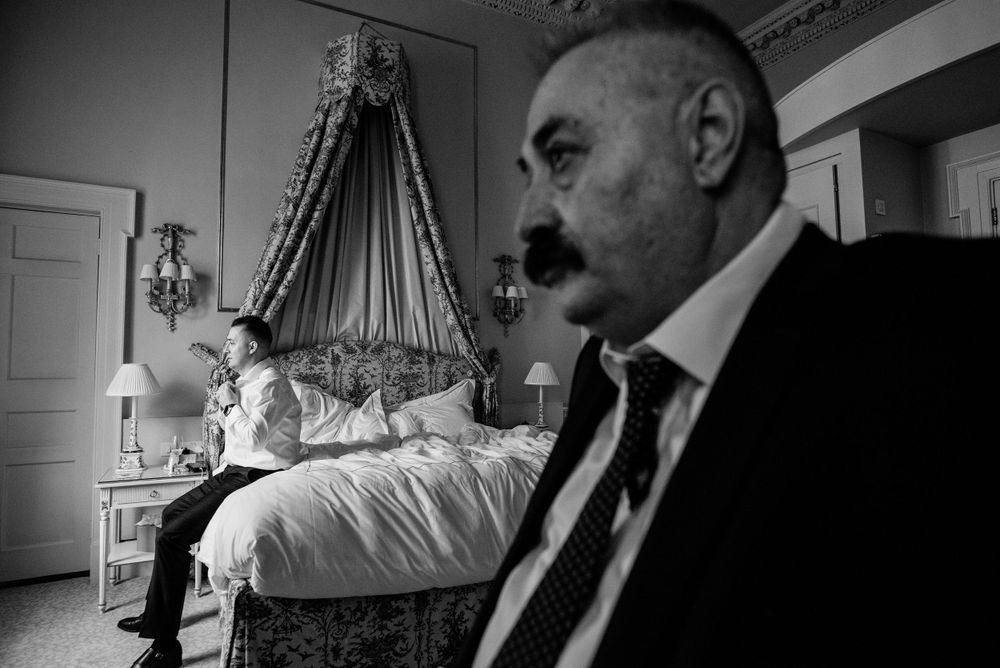 A black and white photograph showing an elegantly decorated hotel room with a canopy bed and person in a suit.