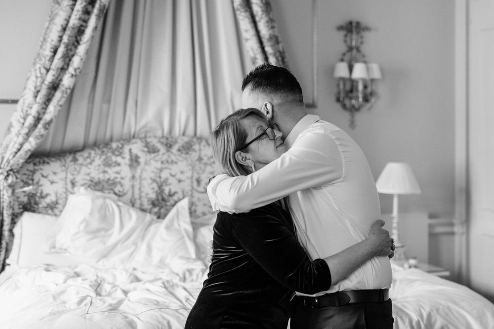 Black and white romantic moment between a couple embracing in an elegant bedroom setting with floral bedding.