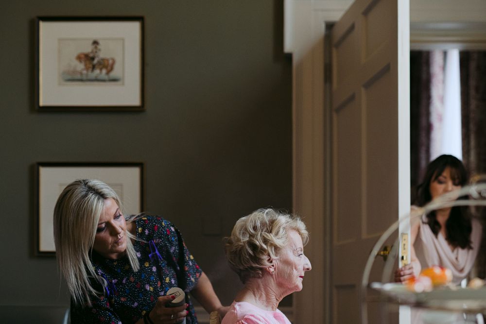 Two people share a quiet moment in a room with framed artwork on the wall during preparations.