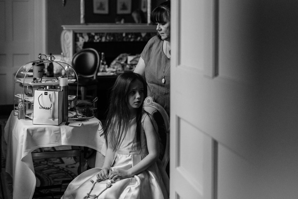 Black and white moody image showing person sitting in a vintage interior setting with antique furnishings in background.