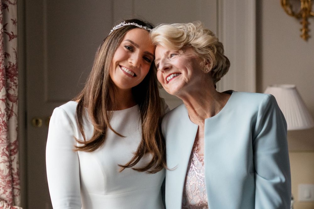 Two people wearing white and light blue outfits share a joyful moment while leaning close together and smiling warmly.
