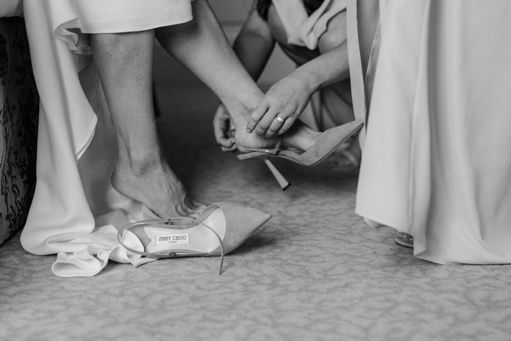Black and white image showing someone helping to tie ballet slippers on a dancer's feet.