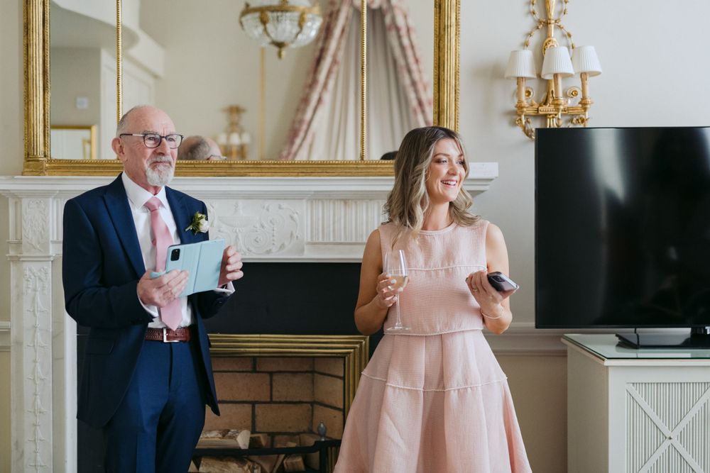 Two well-dressed people stand by a fireplace holding drinks during an elegant indoor celebration.