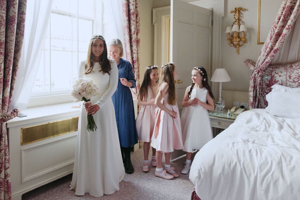 A wedding party getting ready in an elegant white room with floral drapes and vintage decor.