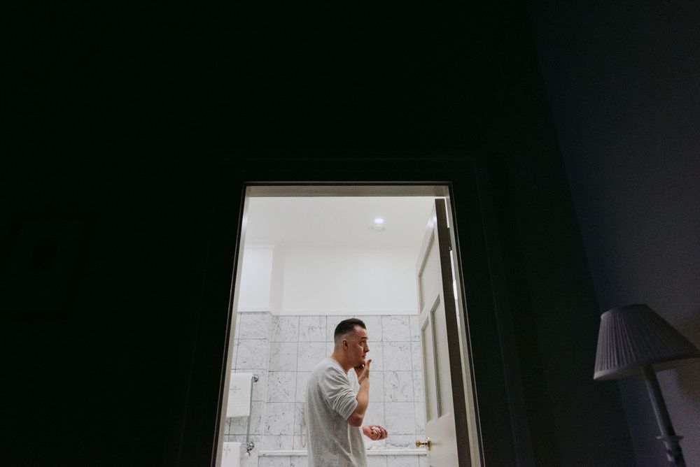 A person stands in a bright doorway against a dark room while brushing their teeth in the morning.