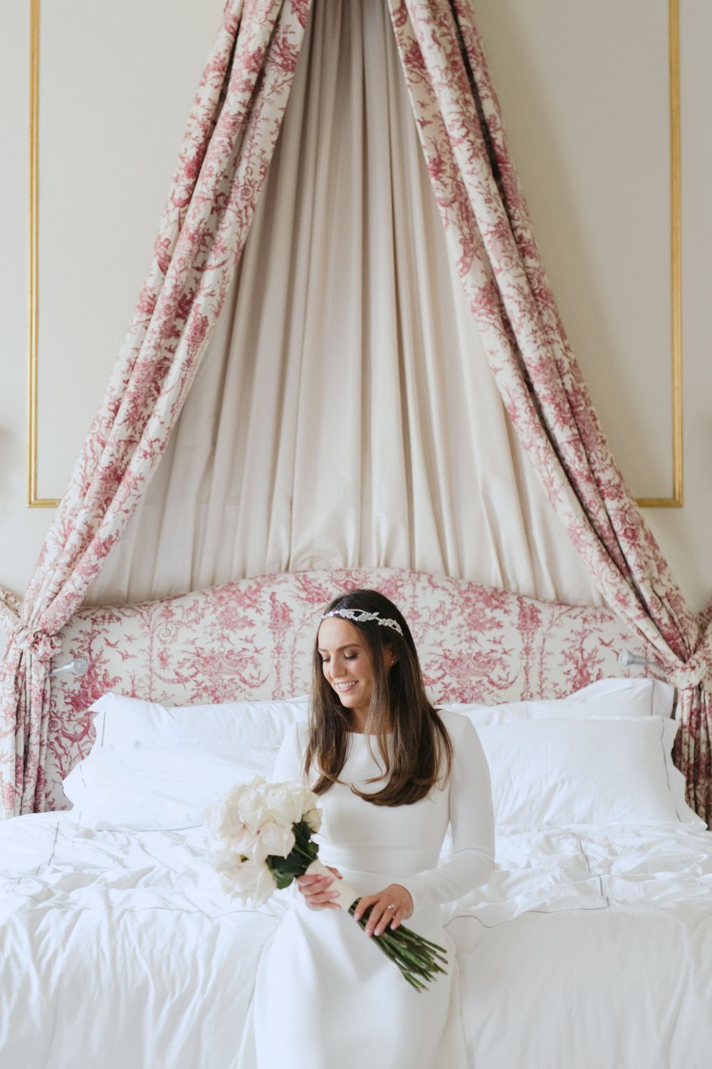 Elegant pink and white toile canopy bed with crisp white bedding and a bridal scene featuring a classic white wedding gown.
