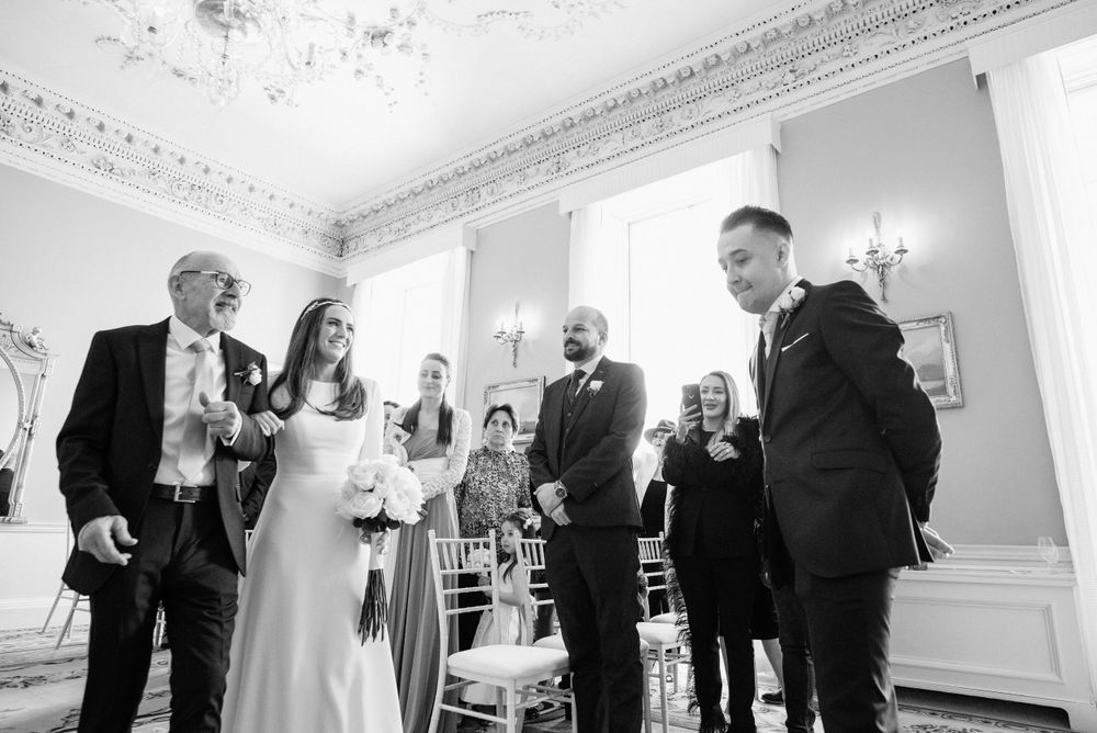 A wedding moment captured in an elegant room with ornate moldings and chandeliers.
