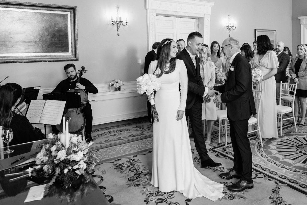 Classical musicians perform during an elegant indoor wedding ceremony with floral decor and candle-lit wall sconces.