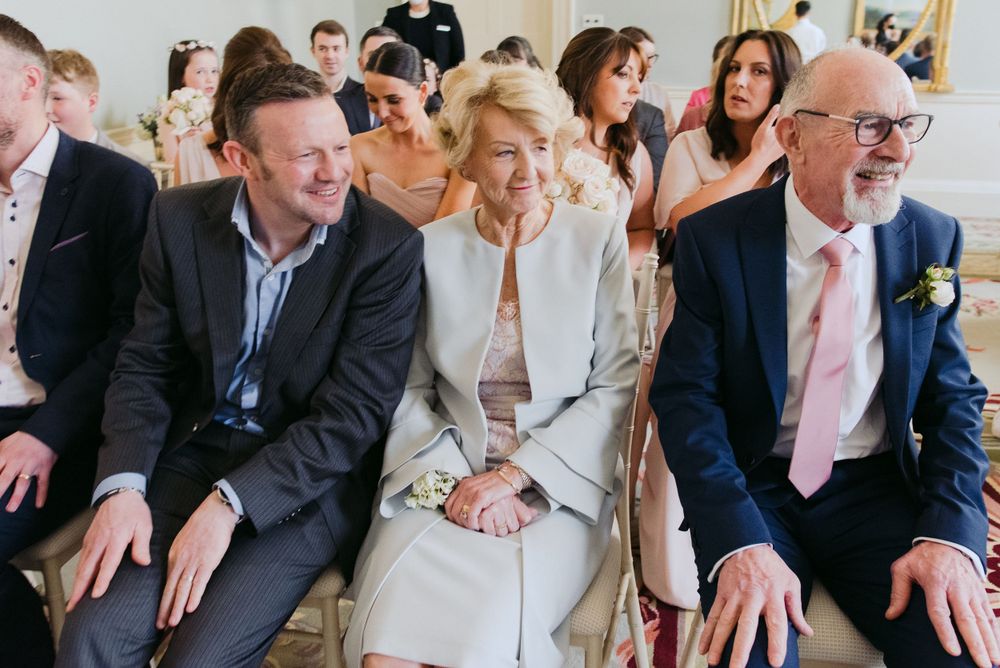 Wedding ceremony guests seated in rows share genuine laughter during a joyful moment at an indoor venue.