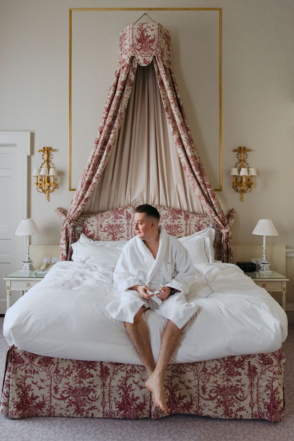 Luxurious canopy bed with red and white toile fabric and a plush white bedspread in an elegant hotel room setting.
