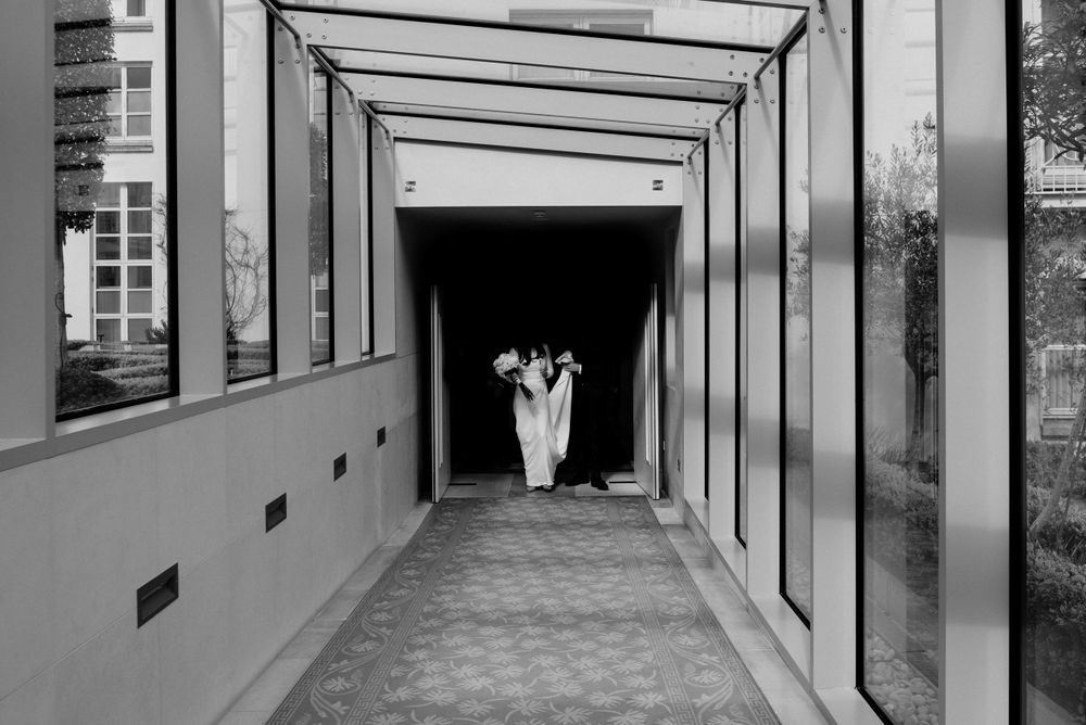 A black and white corridor with geometric architectural lines leads to silhouettes at the end of a tunnel-like space.