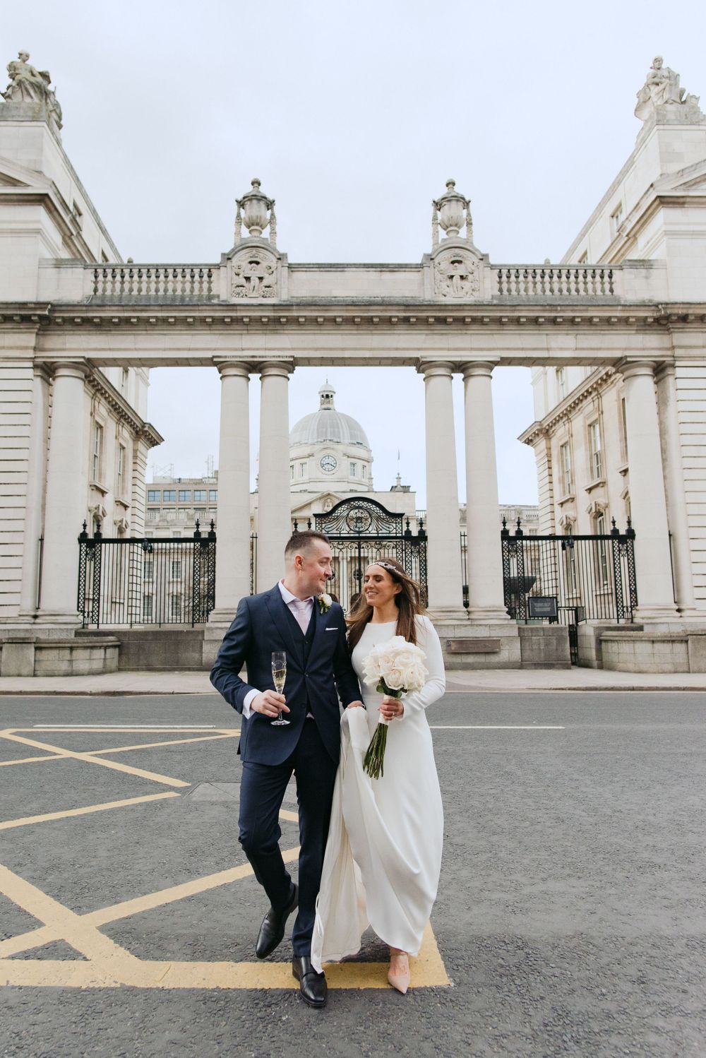 Newlywed pair celebrates with champagne toast at the entrance gates of historic Dublin landmark Trinity College.