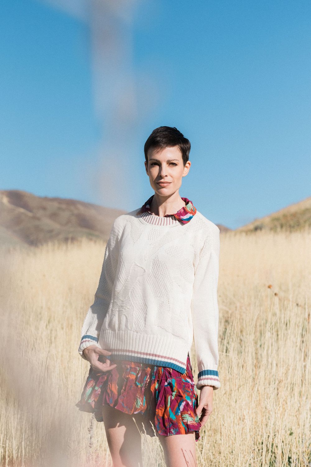 Person in white sweater poses in golden wheat field against blue sky in artistic portrait series.