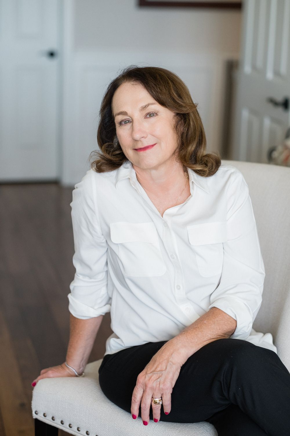 A person in a white button-down shirt and black pants sits casually on a light-colored couch in a bright room.