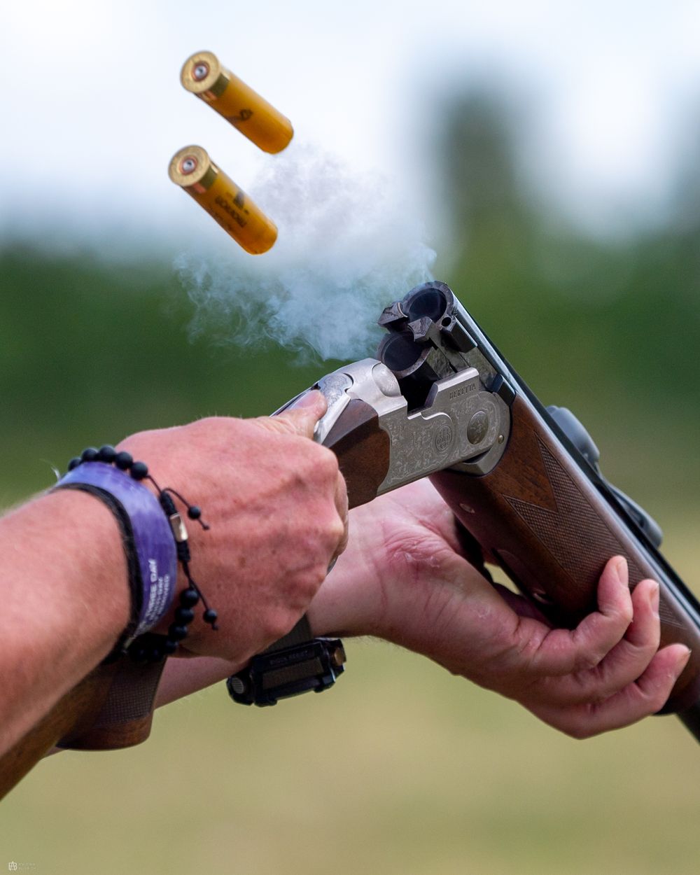 Close-up of cartridges being ejected from an over-and-under shotgun, smoke rising from the chamber during a clay shooting session.