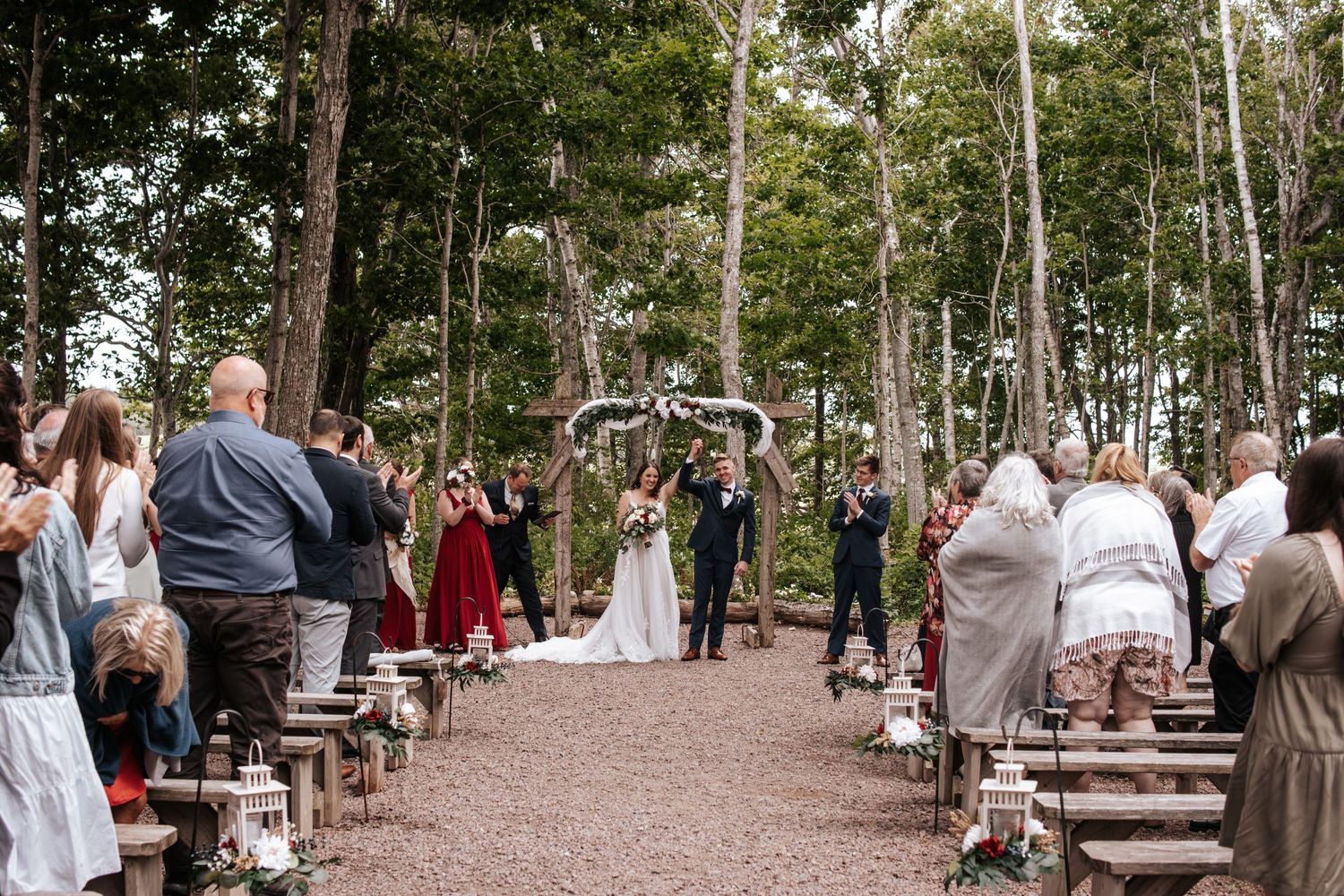 A rustic outdoor wedding ceremony setup with wooden benches in a forest clearing.