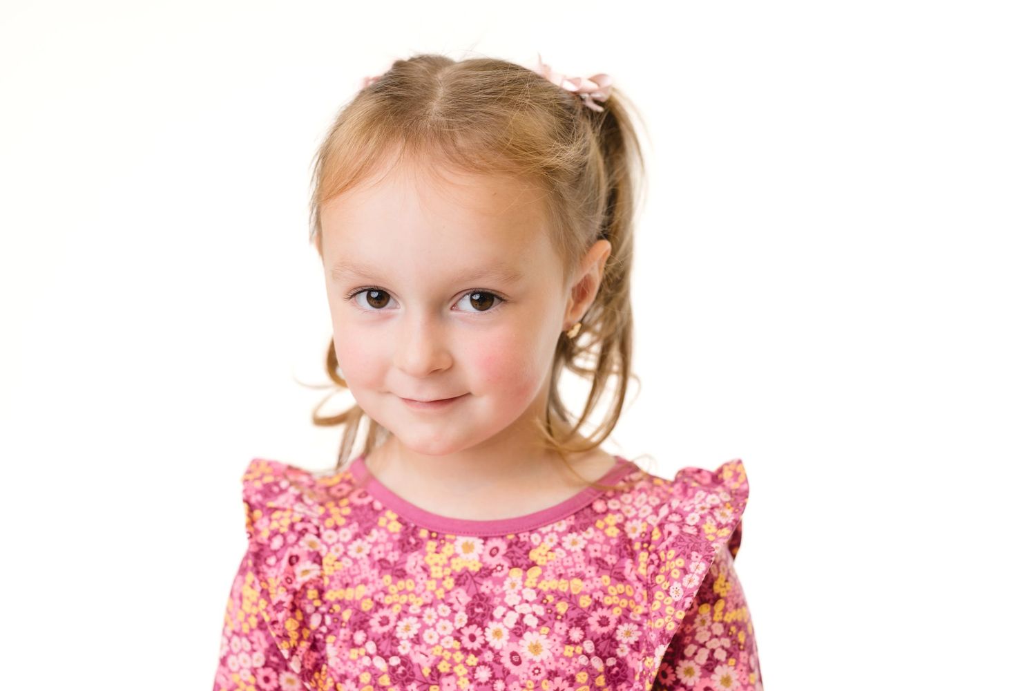Portrait of a young girl student wearing a pink floral dress while posing against a white background.