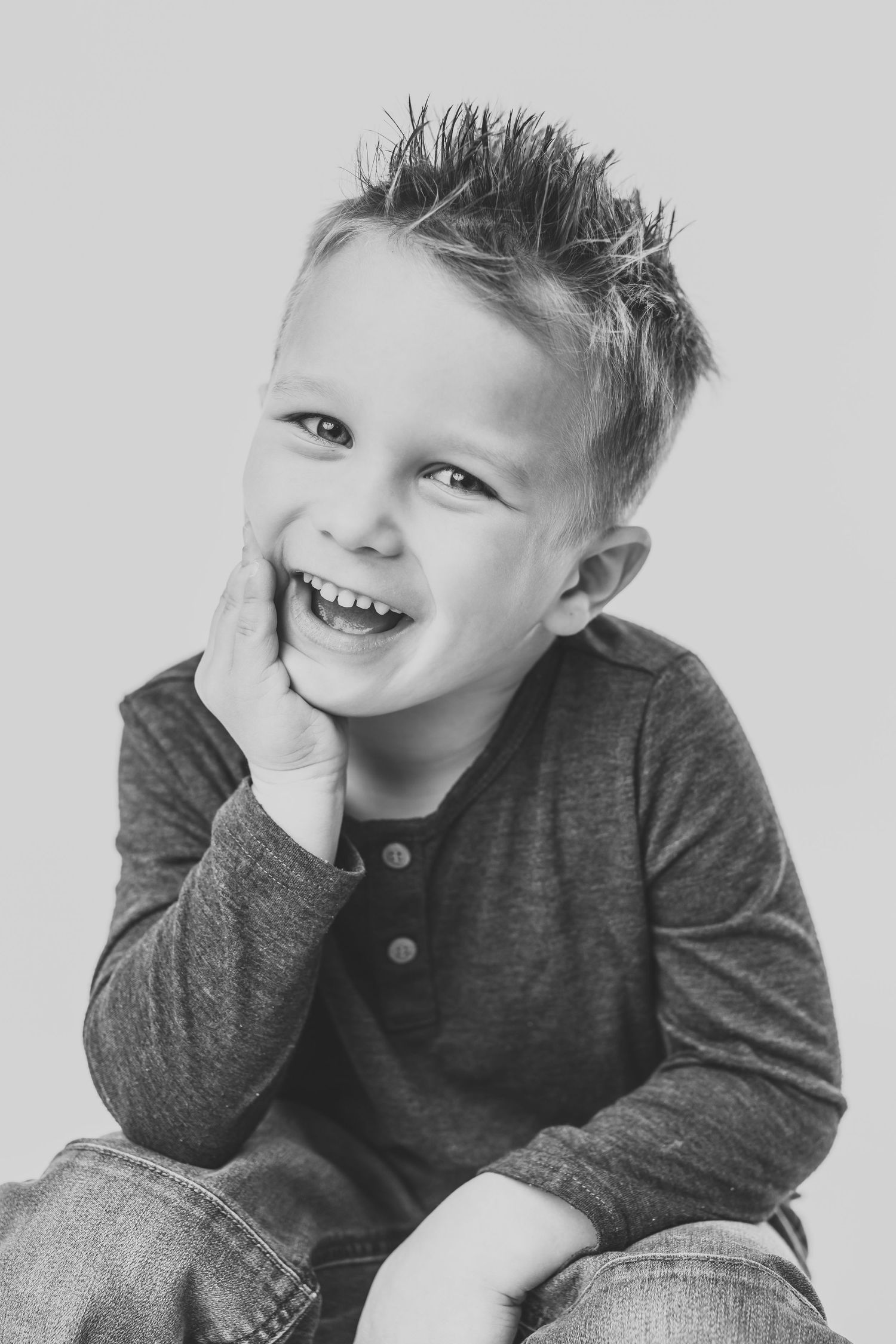 A series of black and white portraits showing a young child in a gray henley shirt making playful expressions.