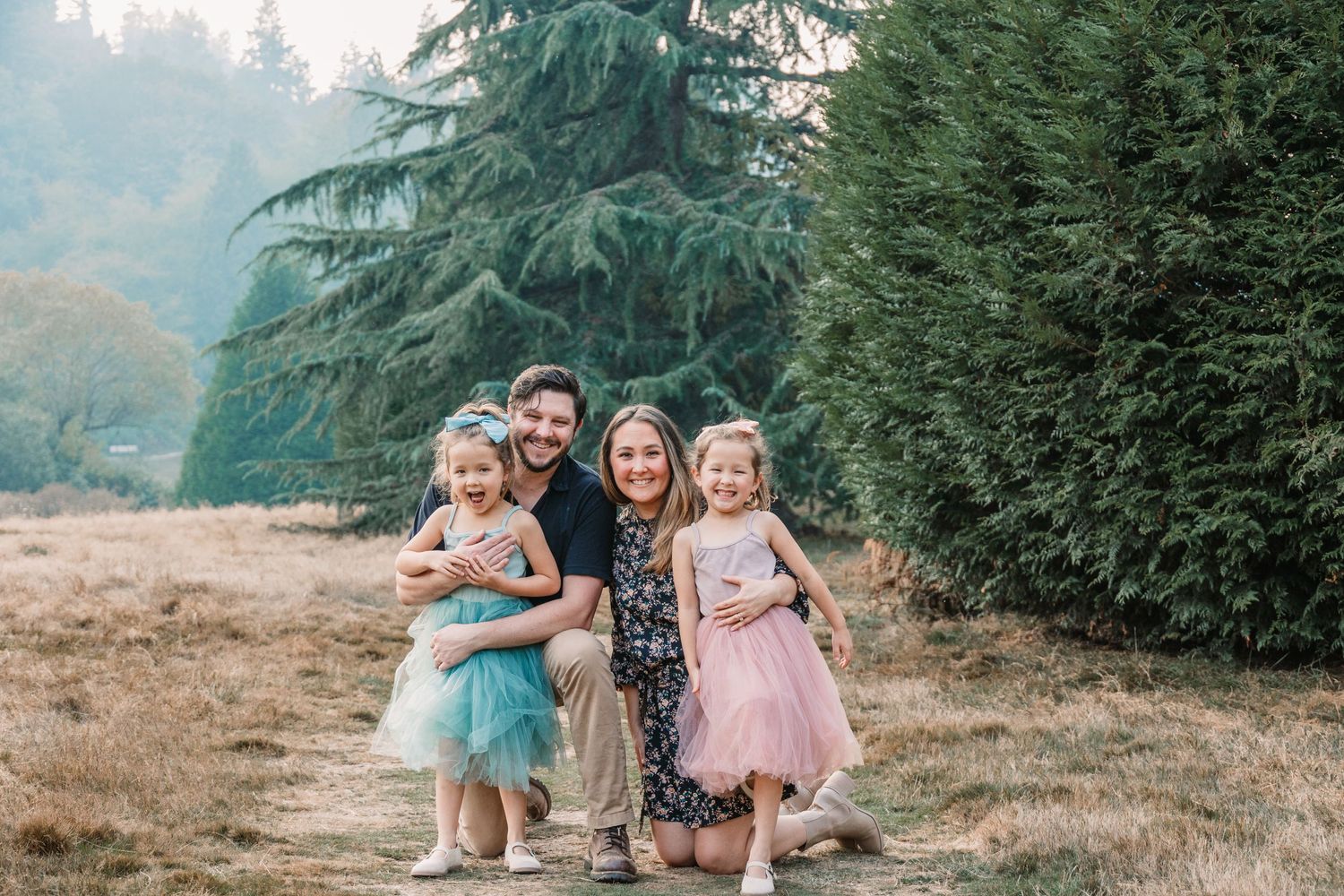 A happy family portrait with children in tulle dresses against an evergreen backdrop.