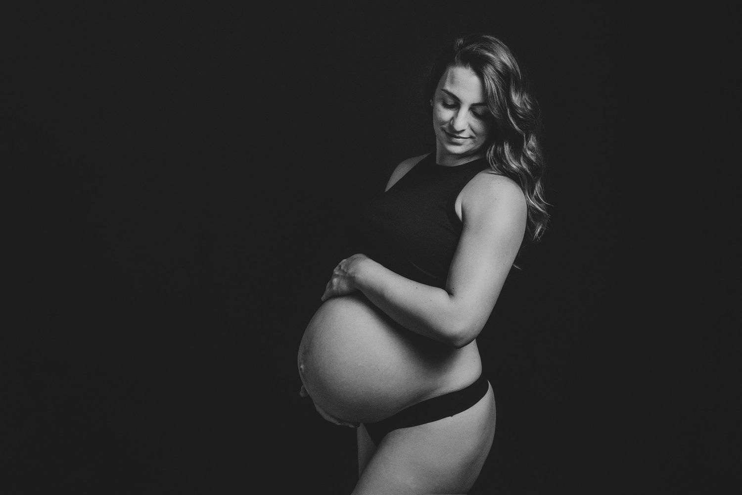 expecting mother to be with styled curly hair whose into fitness wearing black lovingly holding her pregnant belly