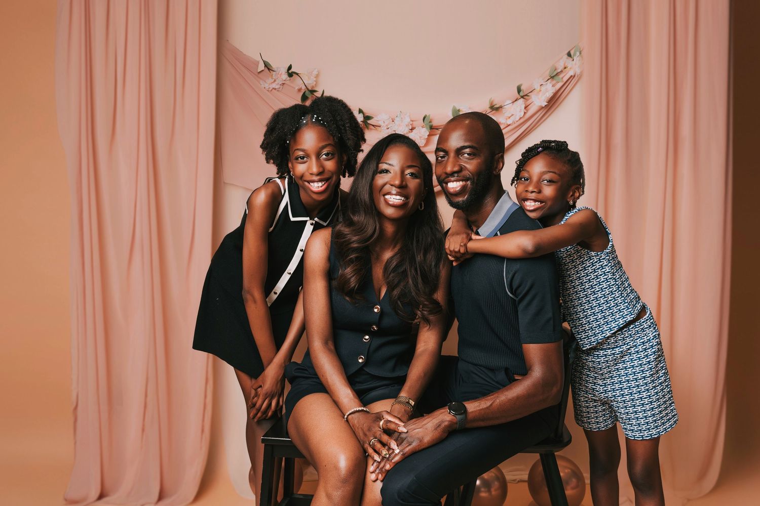 A family in coordinated black and blue outfits poses together against a neutral backdrop in a studio setting.