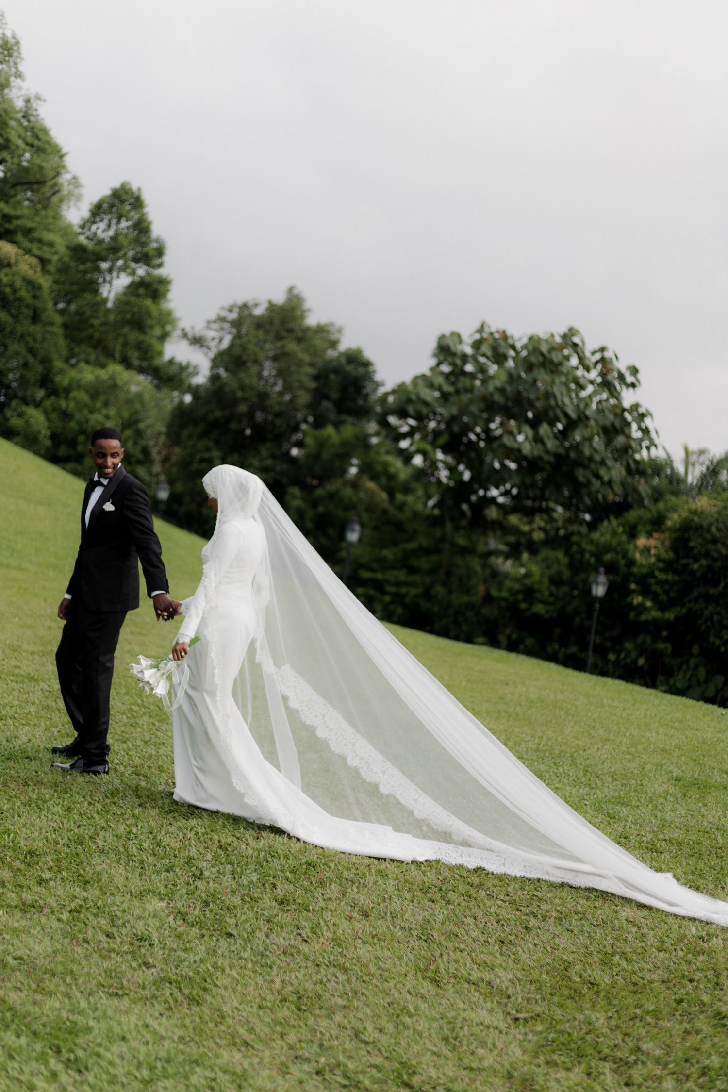 A romantic couple embraces on a brick pathway surrounded by green foliage.