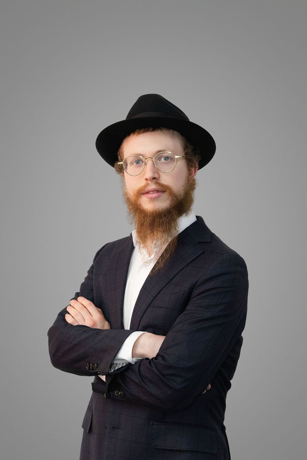 Orthodox Jewish man with red beard wearing black suit and hat poses against gray background in studio portraits.