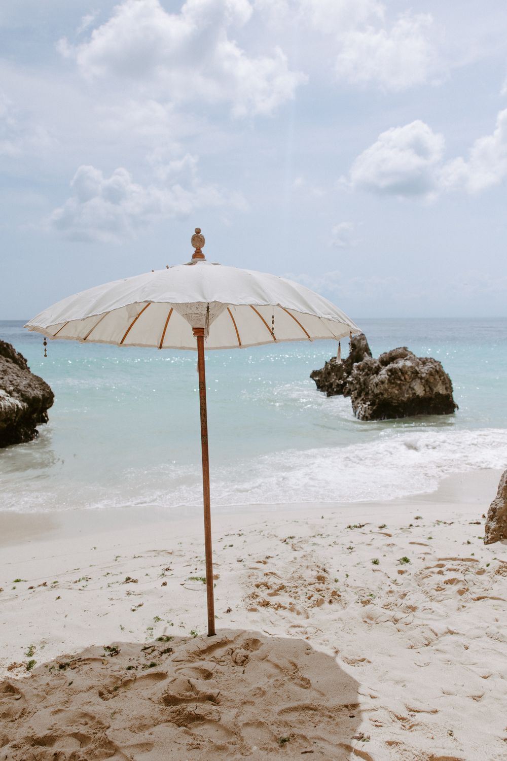White beach umbrellas set up on sandy beach with rocky formations in background.