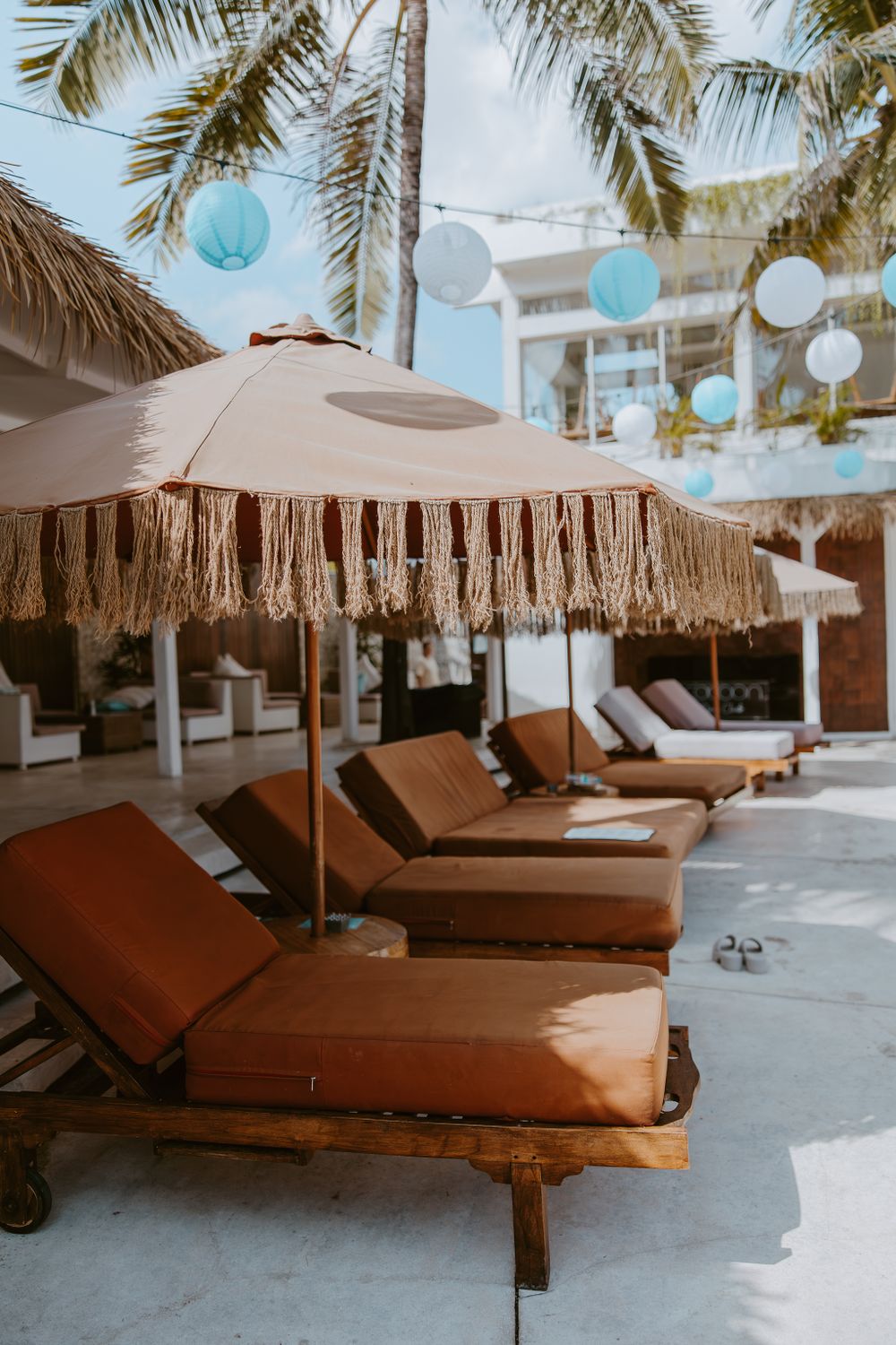 Resort poolside area with thatched umbrellas and brown loungers.