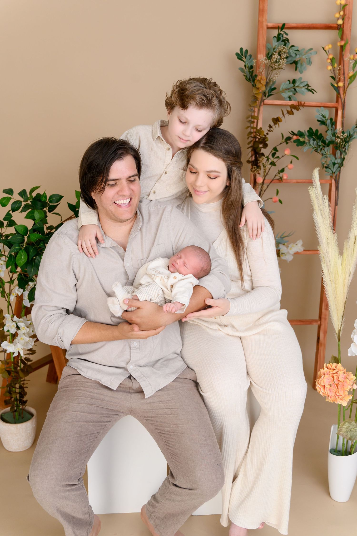 Family photoshoot featuring tender moments in coordinated gray and white outfits against a neutral backdrop with plants.