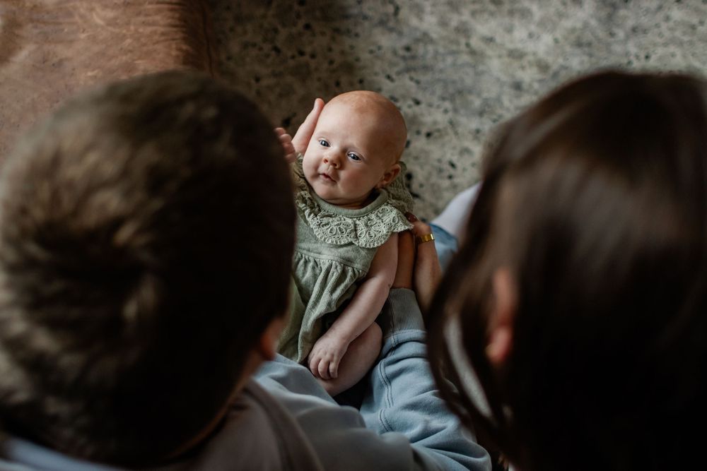 New parents lovingly gazing down at their newborn baby dressed in a green outfit.