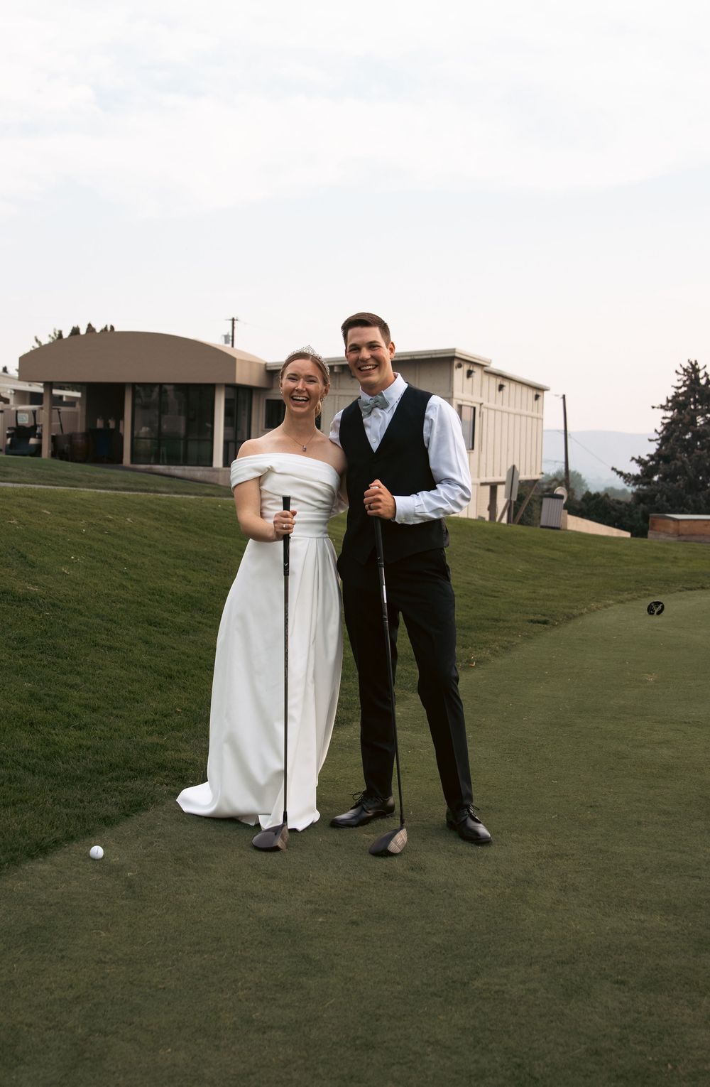 Bride and groom pose together holding golf clubs on a golf course on their wedding day.