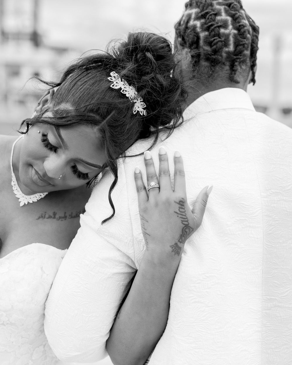 Black and white portrait of a bride snuggling against her groom at a wedding, showing her delicate lace hairpiece and dress.
