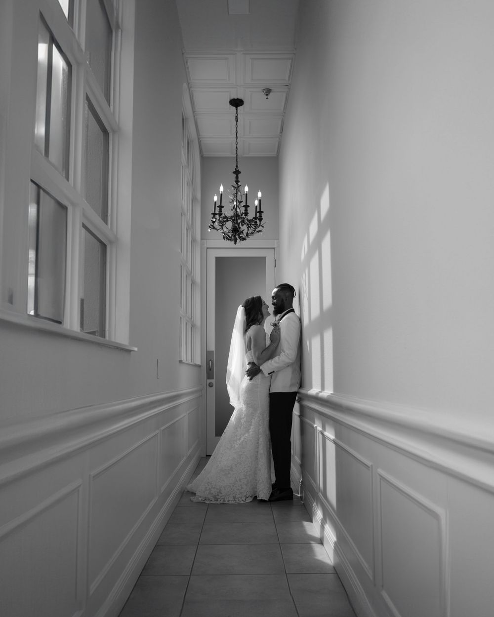 Elegant hallway with chandelier and wainscoting captured in black and white photography.