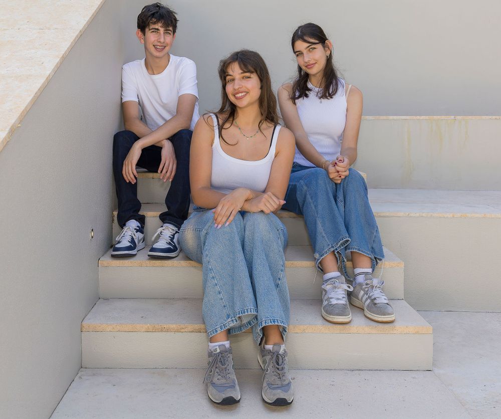 Three people in casual white tops and jeans sit together on concrete steps.